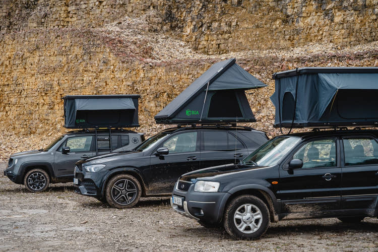 Three vehicles with open BIA roof tents in front of a rock face